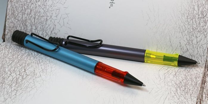 lamy_2025_special_edition_al_star_denim_and_aubergine_ballpoint_pens_on_notebook