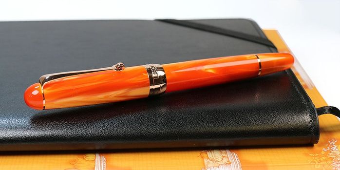 penlux_masterpiece_delgado_tangerine_fountain_pens_capped_on_black_notebook